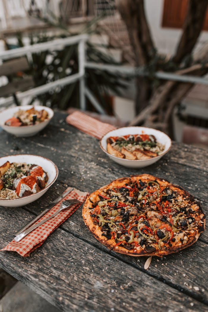 Rustic vegan pizza with healthy bowls on a wooden table outdoors. Perfect for lifestyle and food themes.